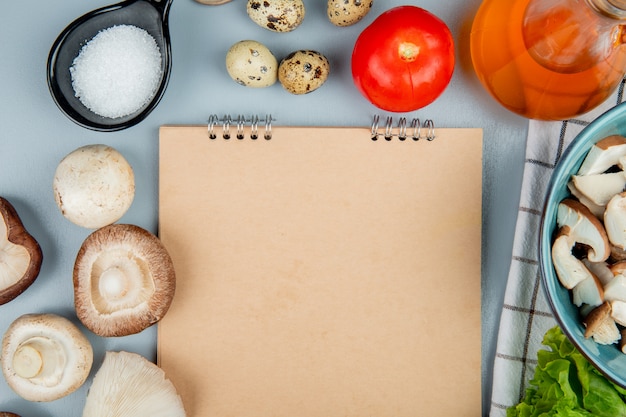 Top view of fresh mushrooms with tomatoes quail eggs and salt arranged around a sketchbook on light blue