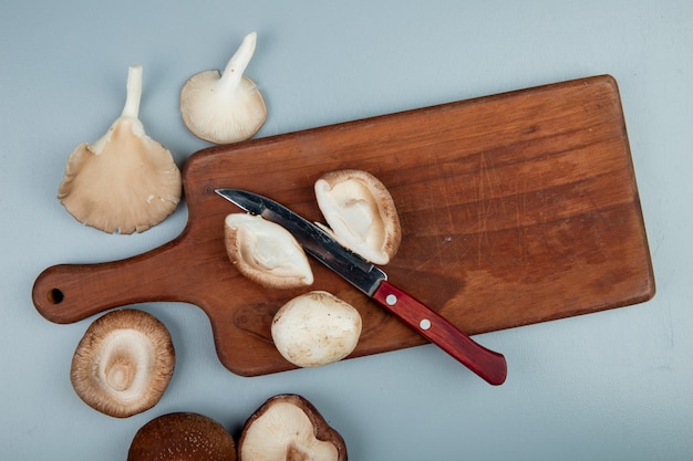 Free Photo top view of fresh mushrooms on a wood cutting board with kitchen knife on light blue