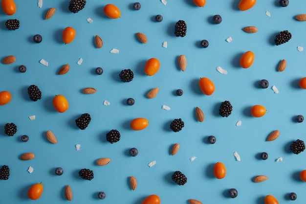 Top view of fresh nutritious cumquat, blueberry, blackberry and almond lying on blue studio background. Summer berries collection and tropical citrus fruit. Organic nutrition and harvest concept.