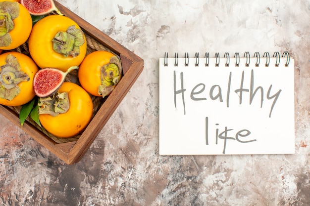 Free Photo top view fresh persimmons cut figs in wooden box healthy life written on notebook on nude background