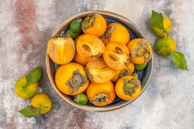 Free Photo top view fresh persimmons feykhoas in a bowl and mandarines on nude background