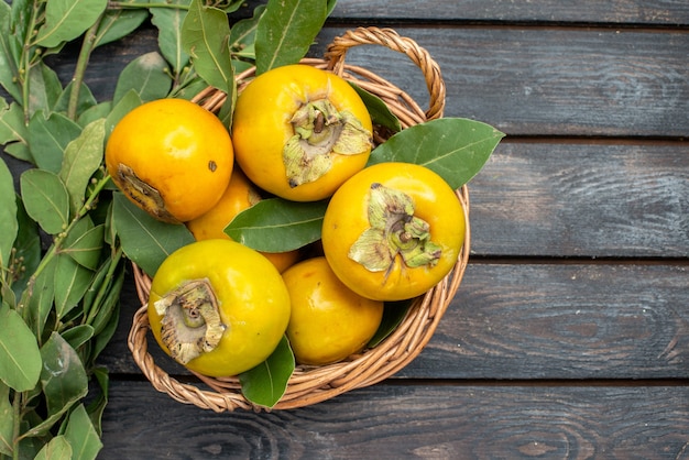 Free photo top view fresh persimmons inside basket on a wooden table, fruit mellow ripe