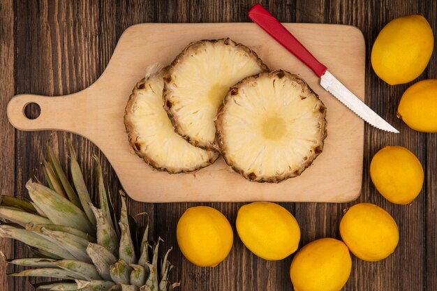 Top view of fresh pineapples on a wooden kitchen board with knife with lemons isolated on a wooden wall