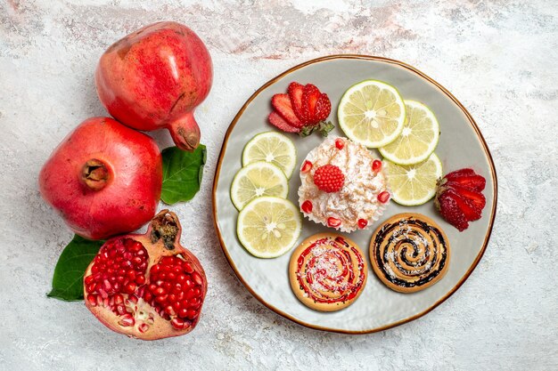 Top view fresh pomegranate with cake and lemon slices on white space