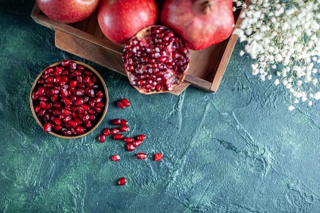 Free photo top view fresh pomegranates on wood serving board small white flowers on table free space