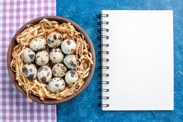 Top view of fresh poultry chicken farm eggs in a tissue basket in a brown bowl on purple stripped towel and spiral notebook on blue background