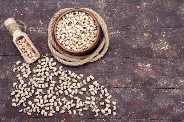 Top view of fresh raw beans inside and outside brown bowl spread all over the brown, food raw bean haricot