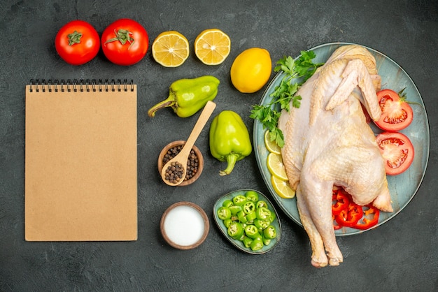 Free photo top view fresh raw chicken with tomatoes lemon and greens on a dark background