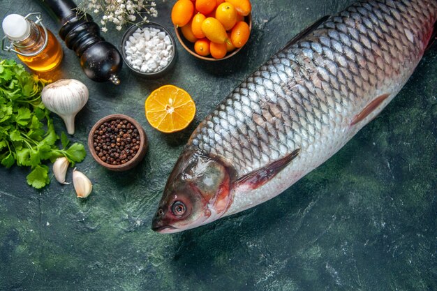 top view fresh raw fish with kumquats and greens on dark background