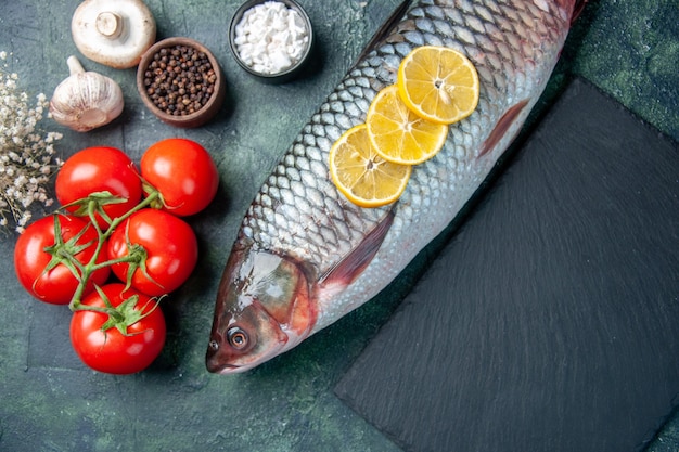 Free photo top view fresh raw fish with lemon slices and tomatoes on dark blue background