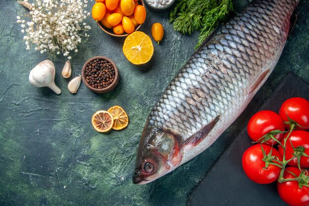 top view fresh raw fish with tomatoes and greens on dark background