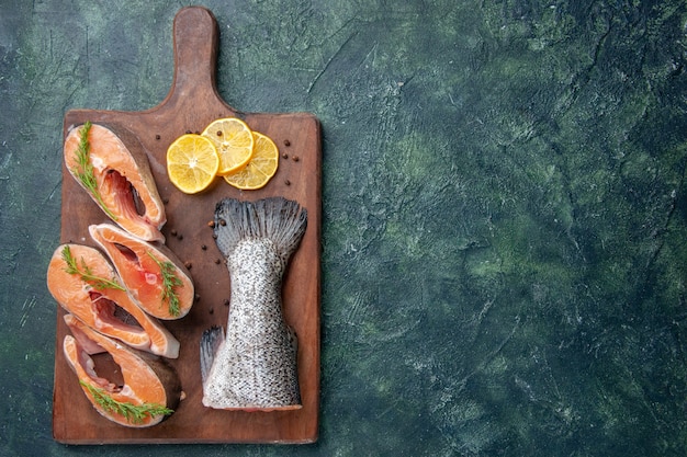 Free Photo top view of fresh raw fishes lemon slices greens pepper on wooden cutting board on the right side on dark mix colors table