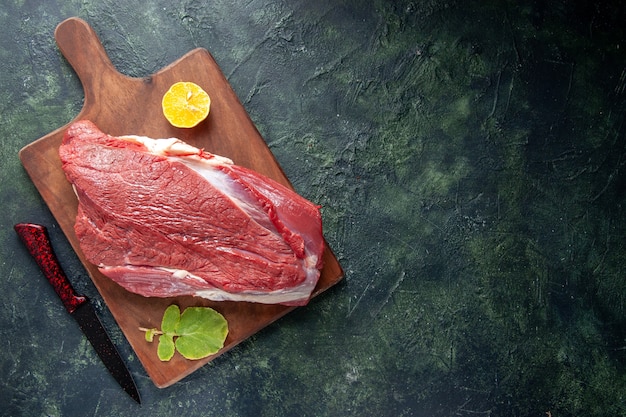 Top view of fresh raw red meats lemon on brown wooden cutting board and knife on dark color background