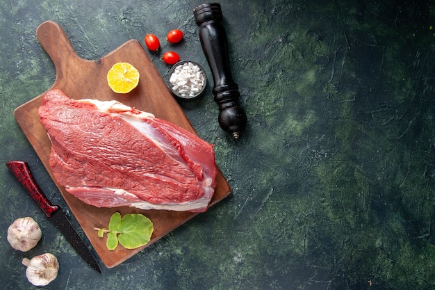 Top view of fresh raw red meats lemon on brown wooden cutting board and knife vegetables wooden hammer on dark color background