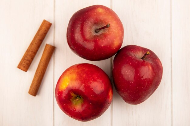 Top view of fresh red apples with cinnamon sticks isolated on a white wooden surface