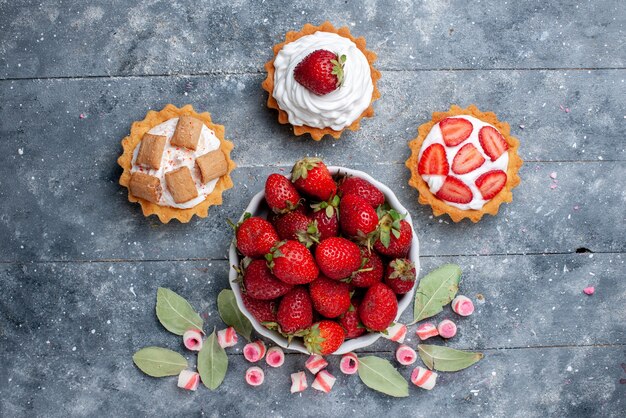 Top view of fresh red strawberries inside plate along with sliced pink candies and cakes on grey, fruit berry fresh mellow