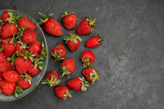 Top view fresh red strawberries inside plate and on grey background