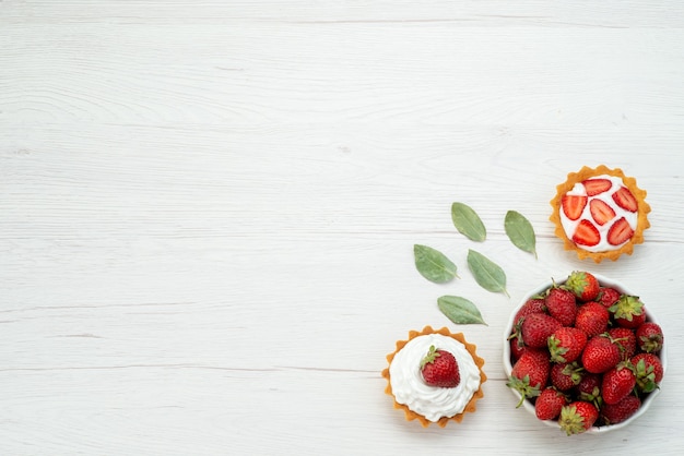 top view of fresh red strawberries mellow and delicious berries inside plate with cakes on light floor fruit berry red fresh