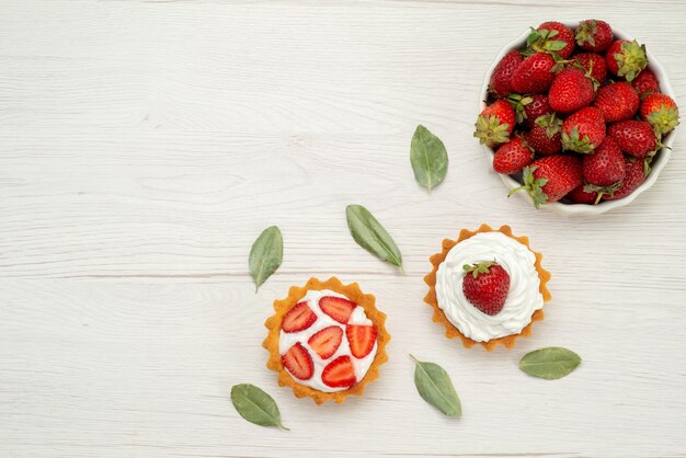 Top view of fresh red strawberries mellow and delicious berries inside white plate with cakes on light, fruit berry red