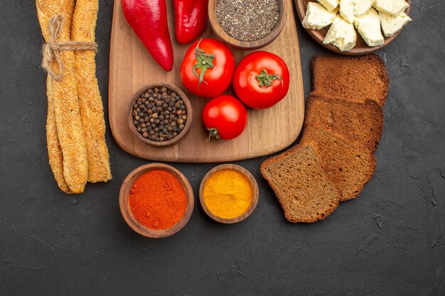 Top view of fresh red tomatoes with seasonings cheese and bread on black