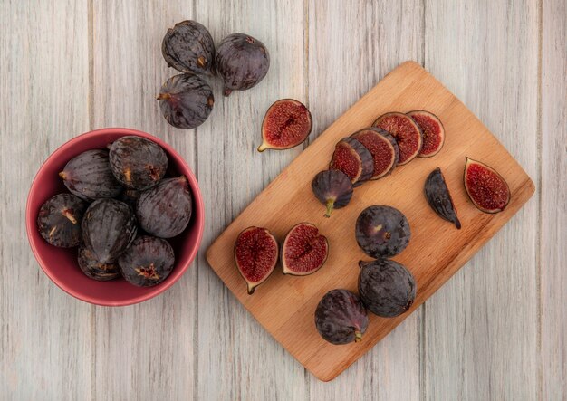 Top view of fresh ripe black mission figs on a wooden kitchen board with black figs on a bowl on a grey wooden surface