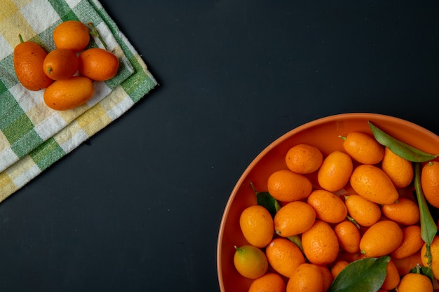 Top view of fresh ripe kumquat fruits on a plate on black with copy space