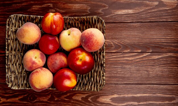 Top view of fresh ripe nectarines and peaches on a wicker tray on wooden rustic table with copy space