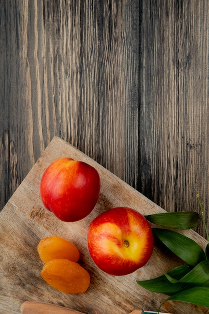 Top view of fresh ripe nectarines with dried apricots on wooden cutting board on rustic background with copy space