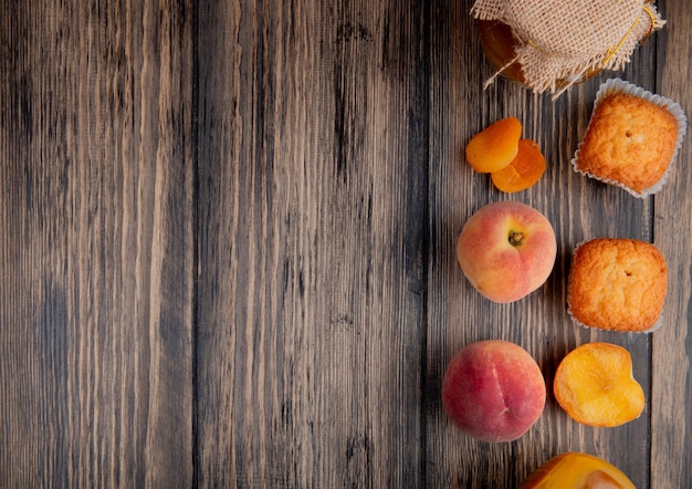 top view of fresh ripe peaches with muffins and peach jam in a glass jar on rustic wooden table with copy space