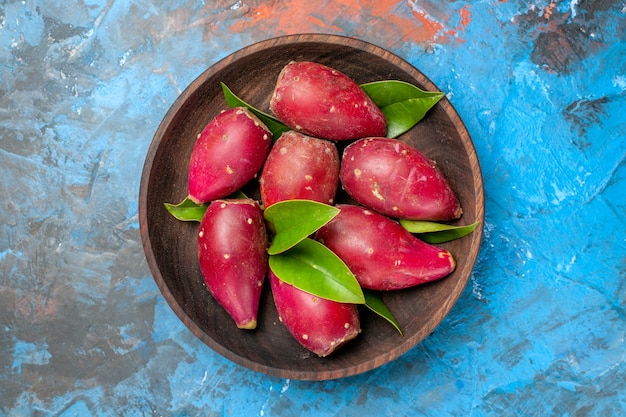 Top view fresh ripe plums inside wooden plate on blue background