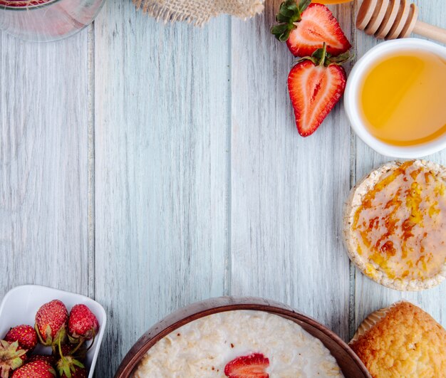 Top view of fresh ripe strawberries honey oatmeal porridge and rice cakes on white wood with copy space