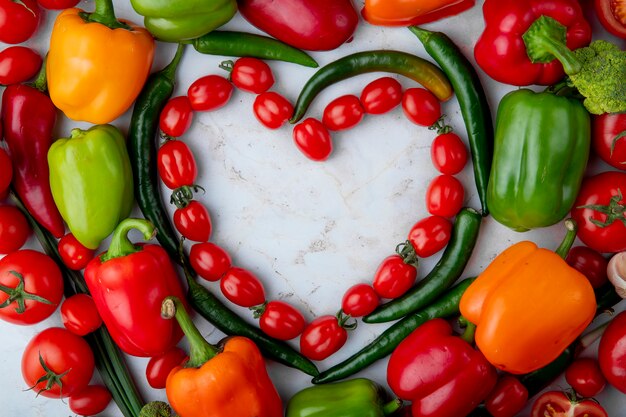 Top view of fresh ripe vegetables arranged in a heart shape cherry tomatoes green chili pepper bell pepper on marble background