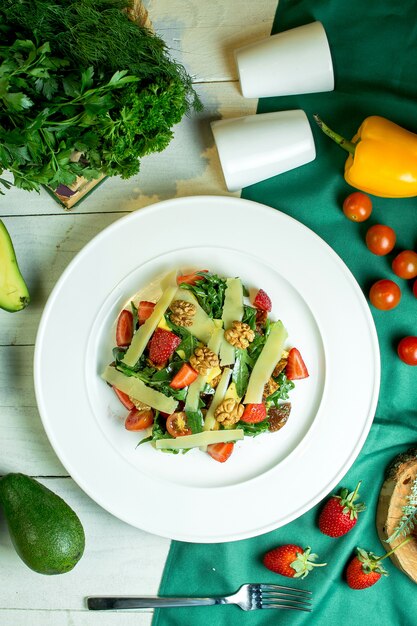 Top view of fresh salad with parmesan cheese walnuts cherry tomatoes and strawberries in a white bowl