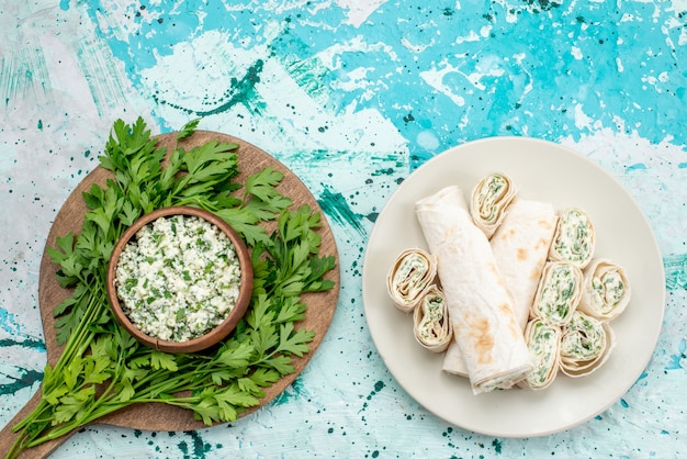 Top view of fresh sliced cabbages salad with greens inside brown bowl and with vegetable rolls on bright-blue desk, food salad freshness snack