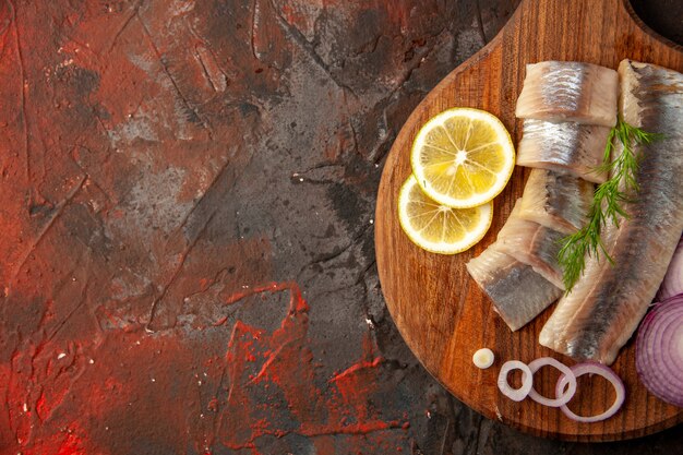 Top view fresh sliced fish with onion rings and lemon on dark background