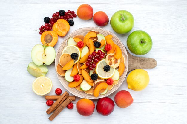 A top view fresh sliced fruits colorful and ripe with whole fruits and cinnamon on the wooden desk and white background fruits color food photo