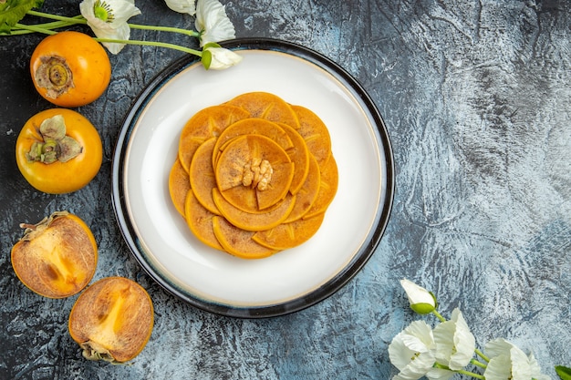 Top view of fresh sliced persimmons inside plate on dark surface