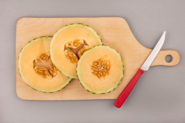 Free Photo top view of fresh slices of cantaloupe melon on a wooden kitchen board with knife on a grey wall