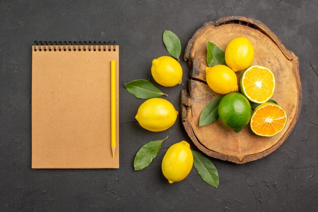 Top view fresh sour lemons with leaves on a dark table yellow fruit lime citrus