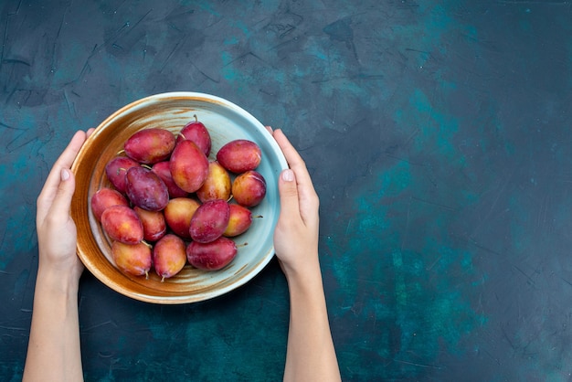 Free photo top view fresh sour plums inside plate on the dark-blue desk sour fresh ripe mellow fruit