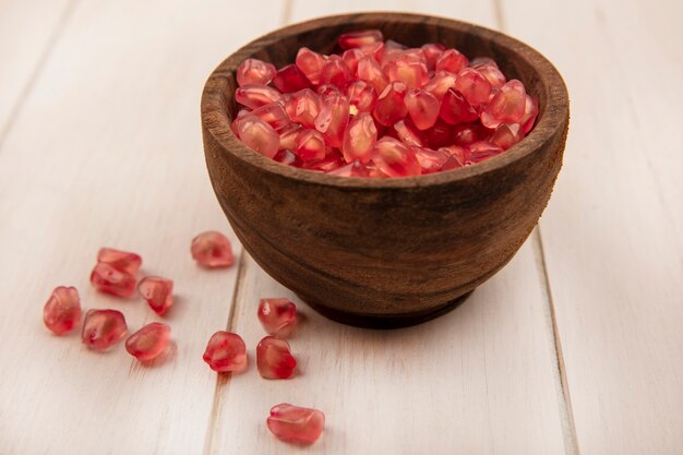 Top view of fresh sweet pomegranate seeds on a wooden bowl with seeds isolated on a white wooden surface