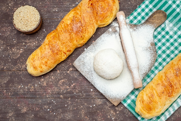 Top view fresh tasty pastry long bun formed pastry on the checkered tissue with flour on the brown wooden desk bun pastry dough bread food meal