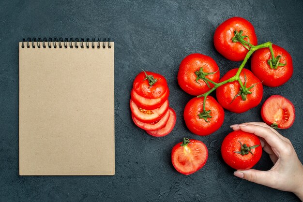 Top view fresh tomato branch chopped tomatoes red tomato in female hand notebook on black table