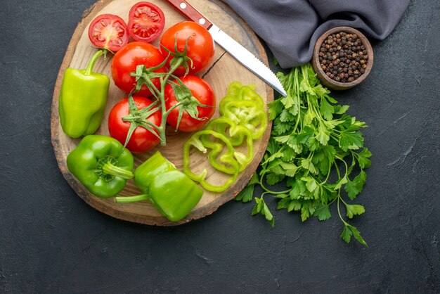 Top view of fresh tomatoes and green peppers on wooden board green bundle on black surface