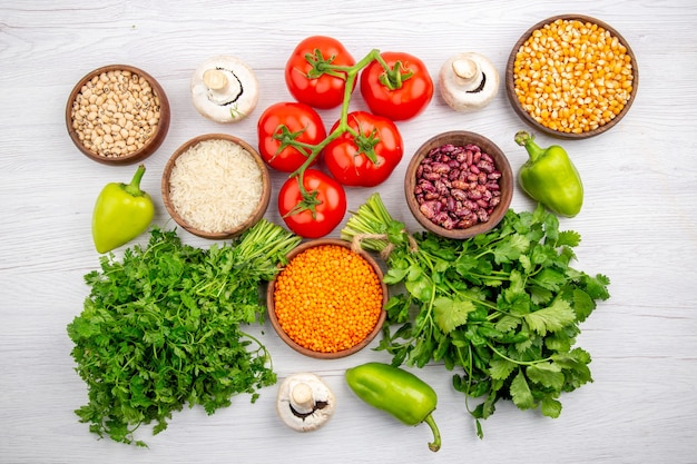 Top view of fresh tomatoes with stem corn kernels beans bundle of greens mushrooms pepper on white background