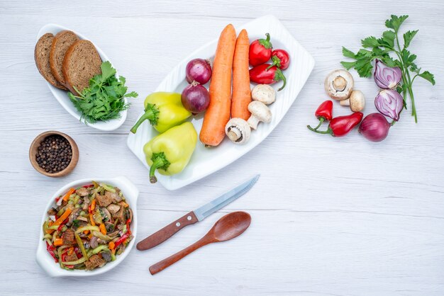 Top view of fresh vegetable salad sliced with meat along with bread loafs and whole vegetables and greens on light desk, food meal salad vitamine