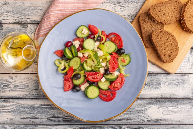 Top view fresh vegetable salad with sliced cucumbers tomatoes olive inside plate with oil and bread on the grey surface vegetable food salad meal color