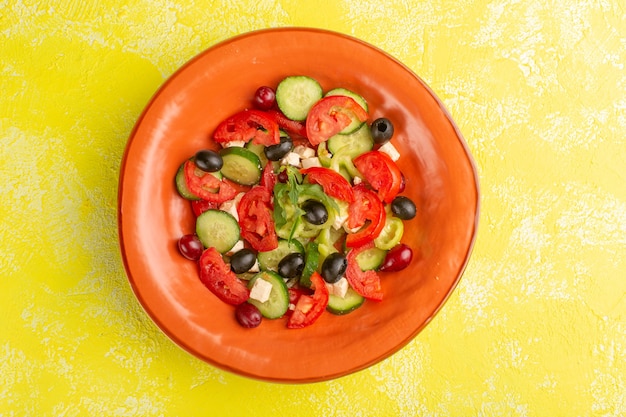 Top view fresh vegetable salad with sliced cucumbers tomatoes olive inside plate on the yellow desk vegetable food salad meal color