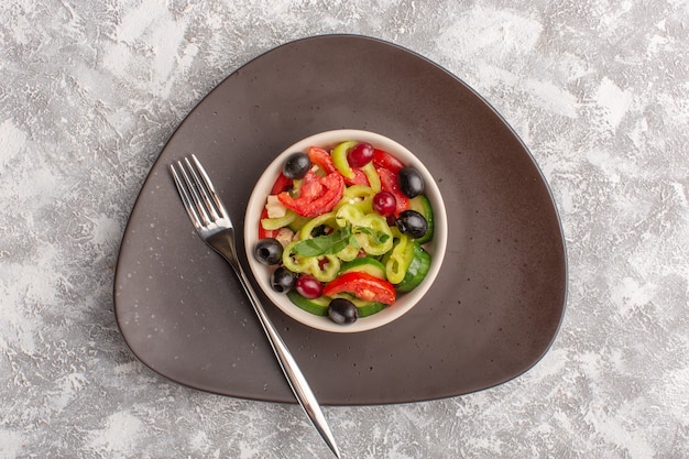 Free photo top view fresh vegetable salad with sliced cucumbers tomatoes olive and white cheese inside brown plate on the grey desk vegetable food salad meal