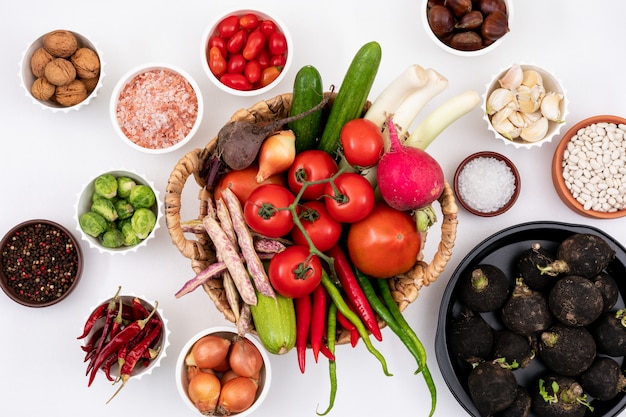 Free photo top view fresh vegetables in basket surrounded by other vegetable in plates and white bowls on white